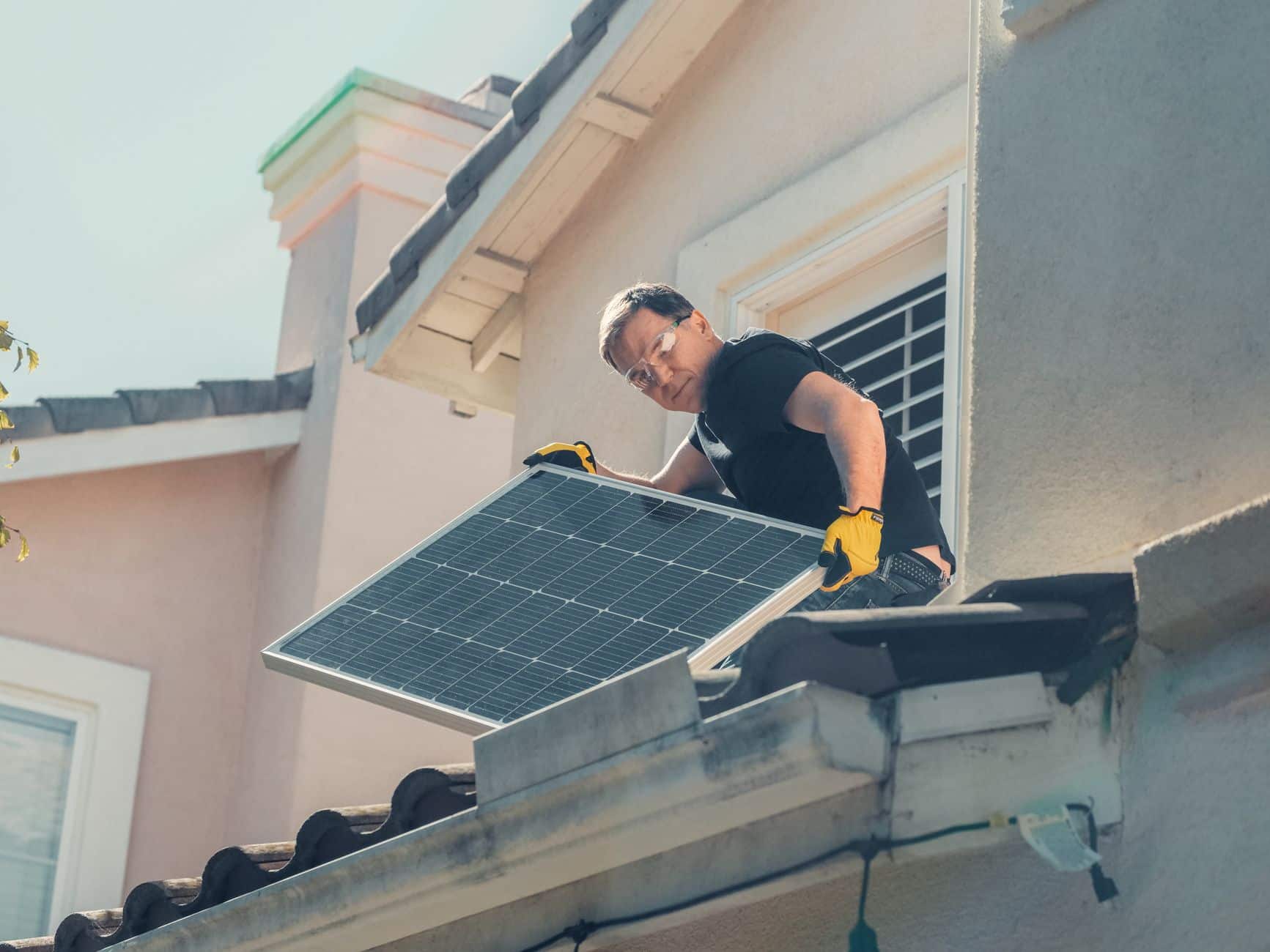 Technician in protective gear installing solar panels on a residential roof