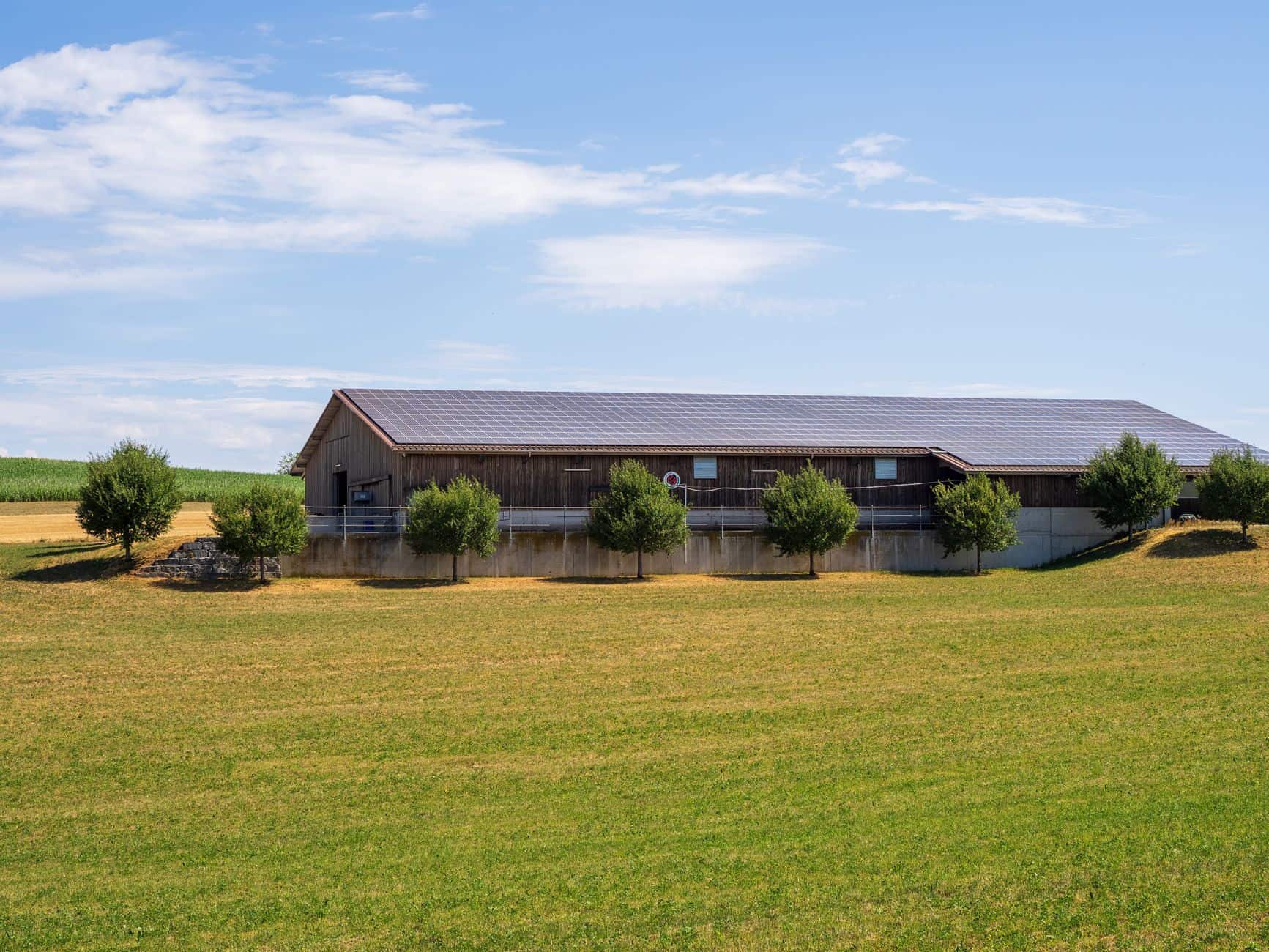 Solar panels mounted on a barn roof in a sunny agricultural field