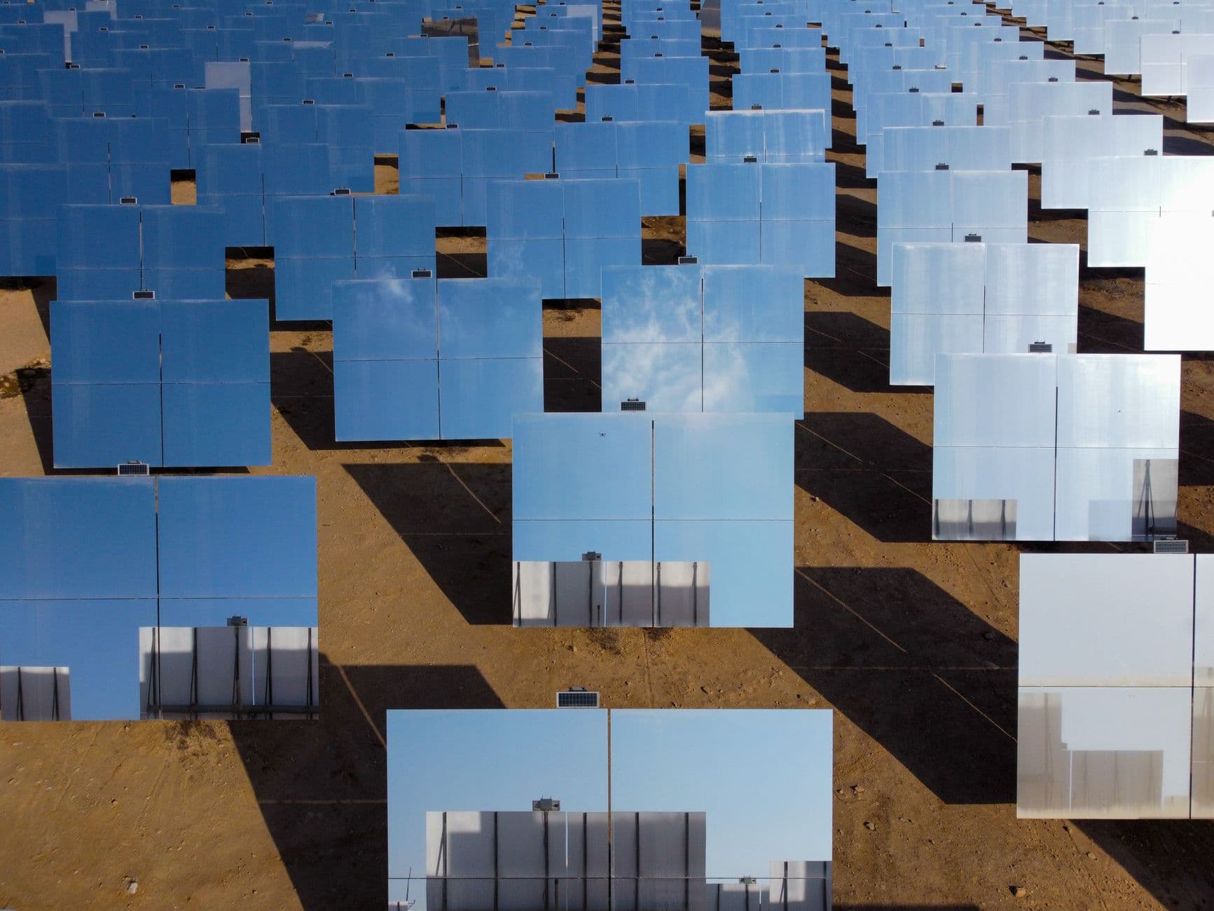 Aerial view of a solar farm with rows of reflective panels in a desert landscape