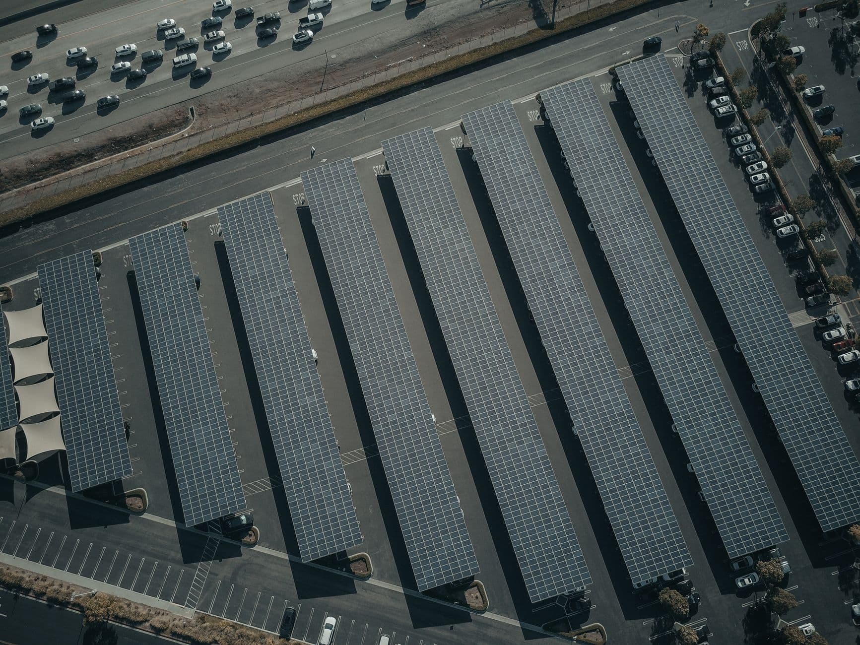 Aerial view of a large solar farm with rows of panels next to a busy parking lot