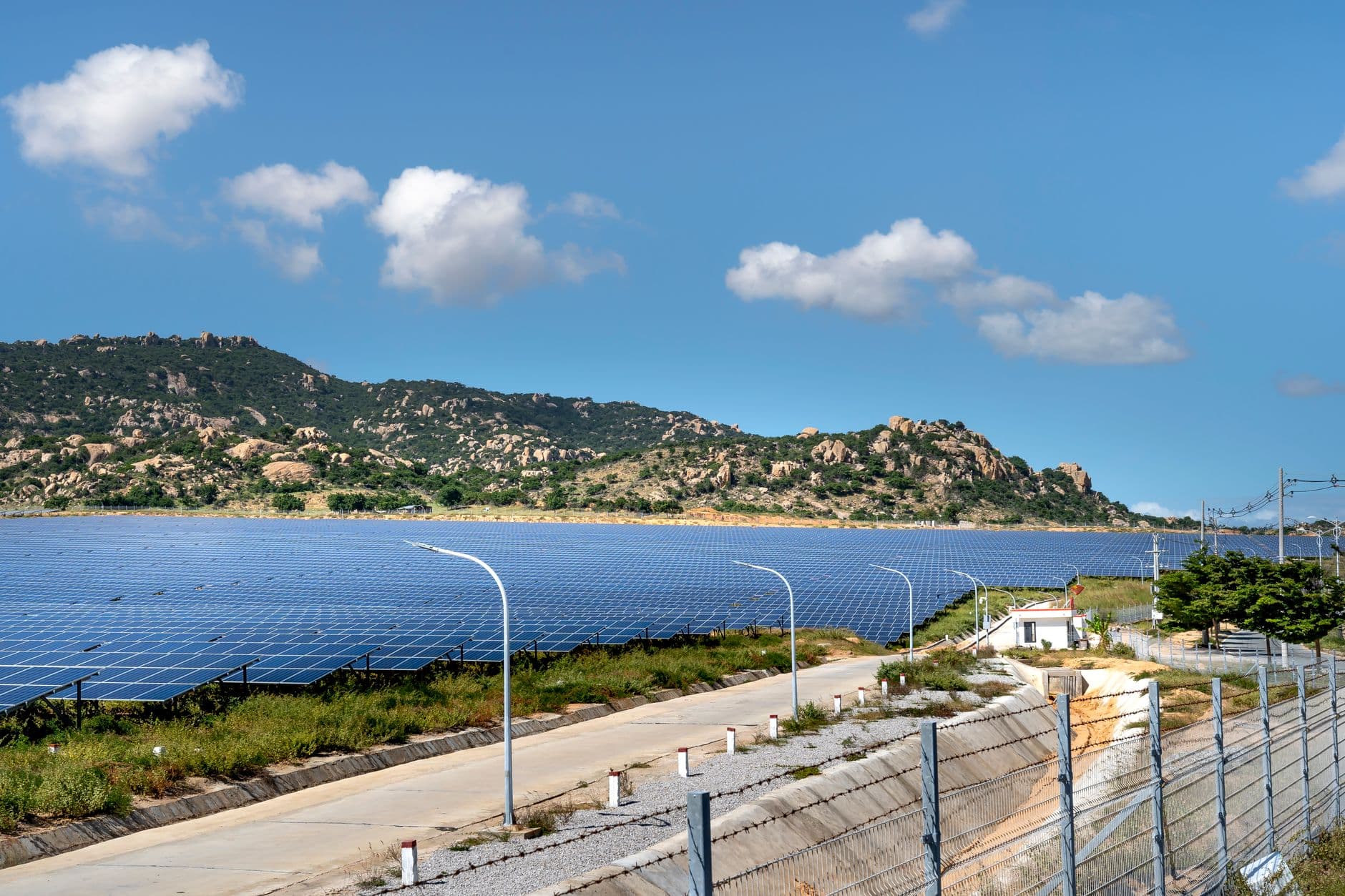 A vast solar farm with panels under a bright blue sky and mountains in the background