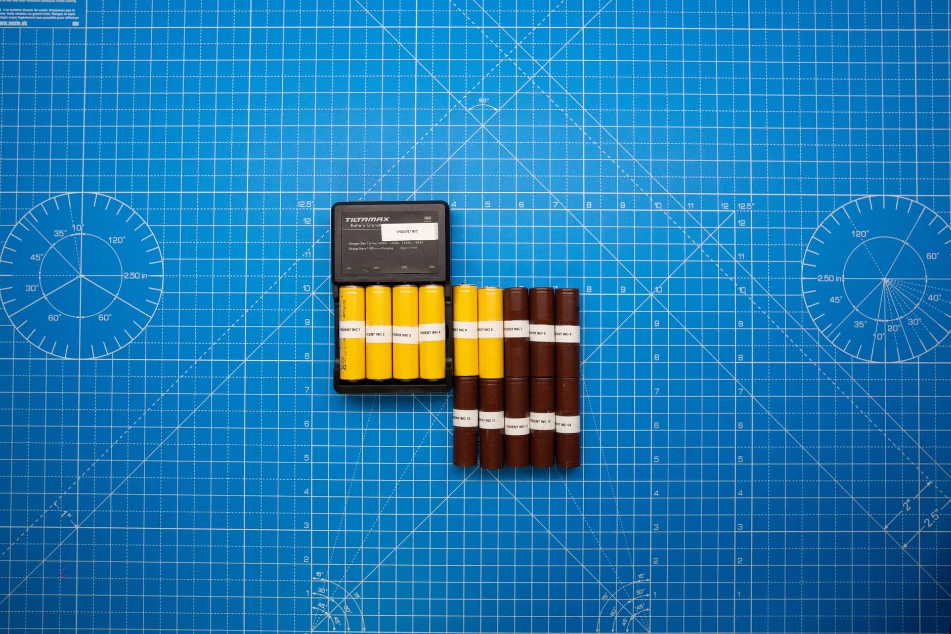Top-down view of battery modules arranged on a blue grid with a charger, illustrating energy storage technology