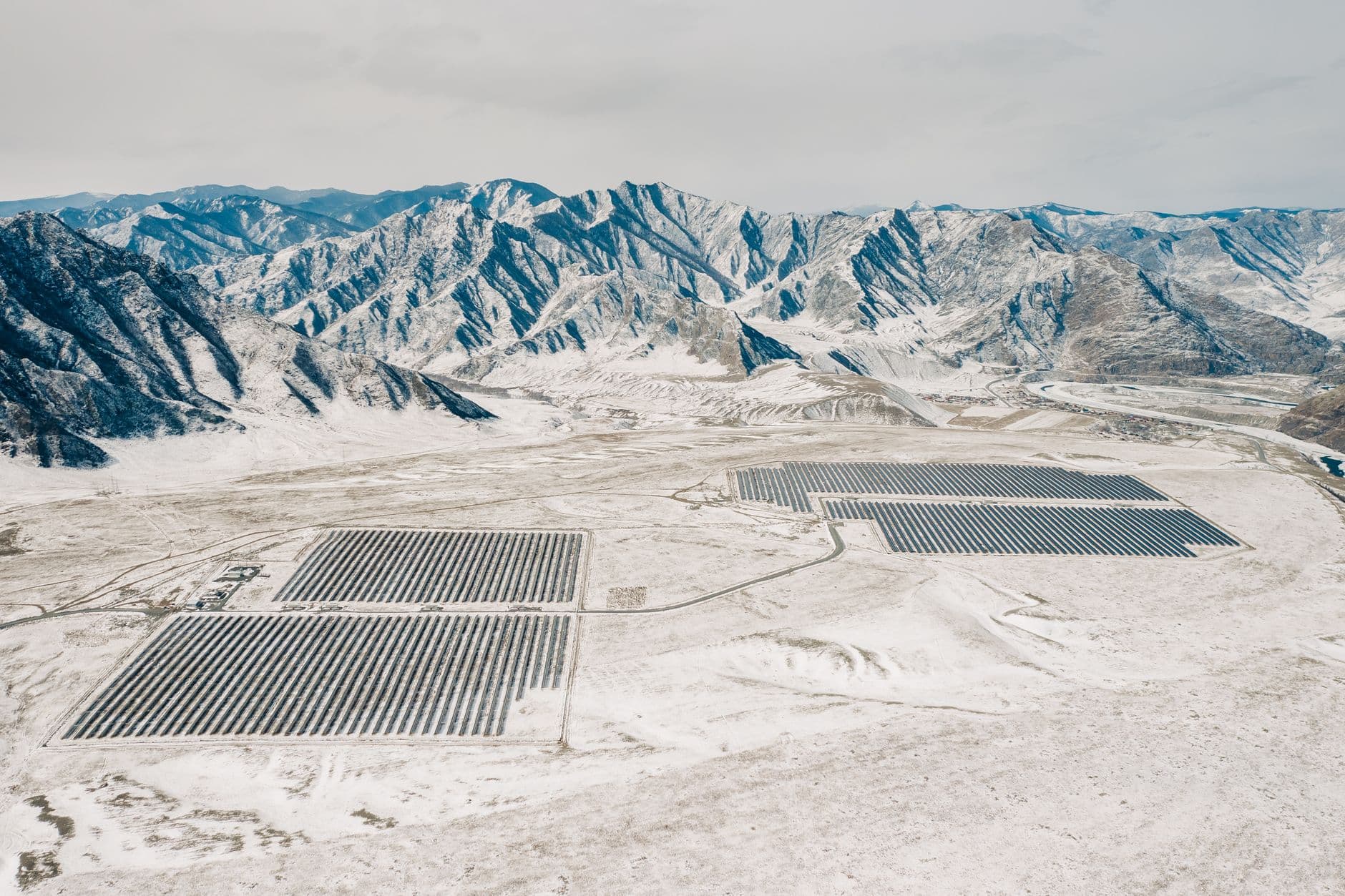 Aerial view of a solar farm surrounded by snow‑capped mountains