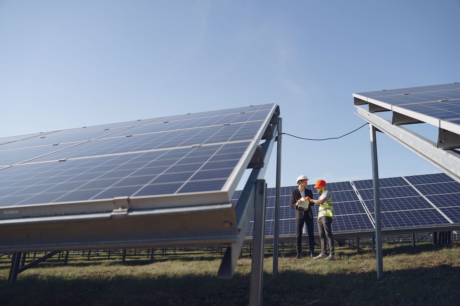 Supervisor in hard hat and formal attire discussing project paperwork beside modern solar panels under a blue sky