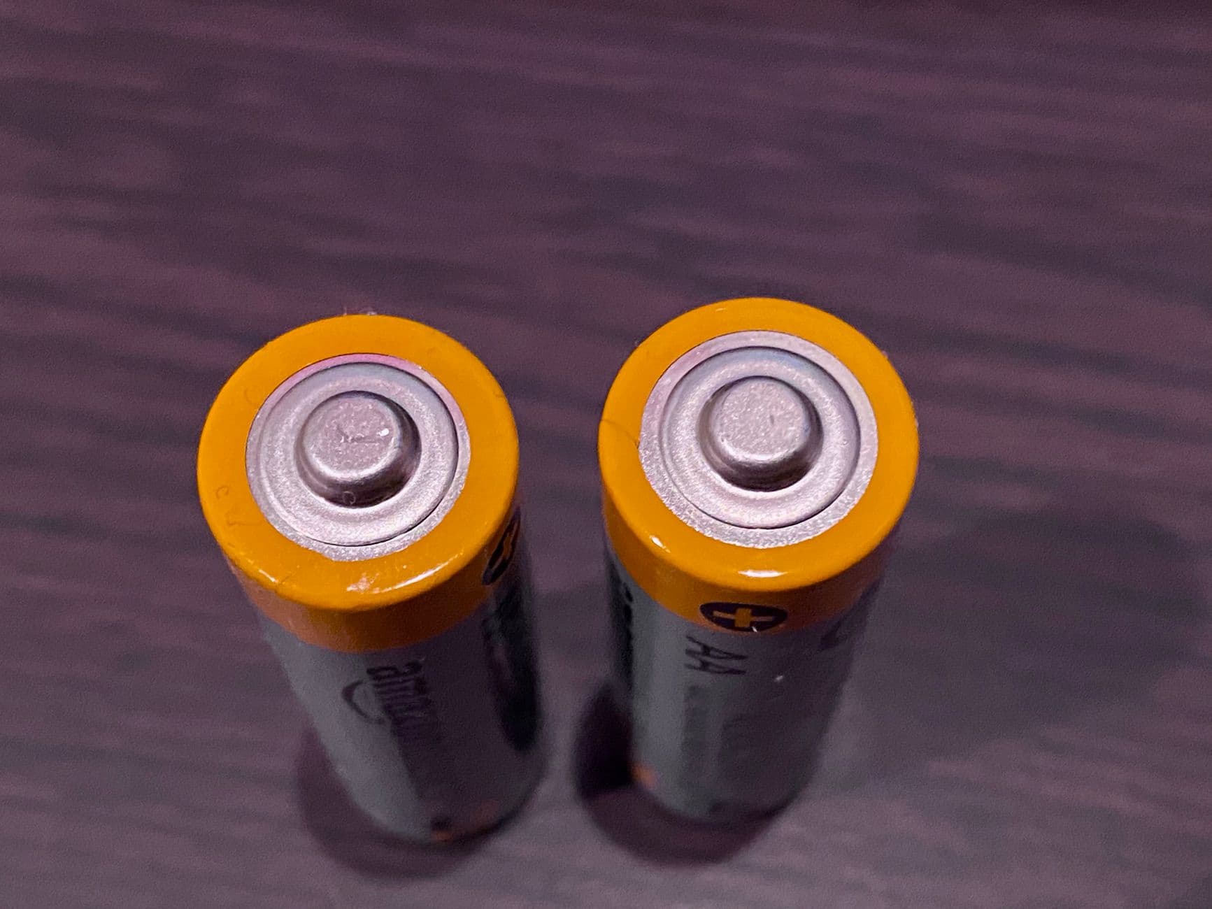 Top view of two AA batteries with yellow tops on a dark surface