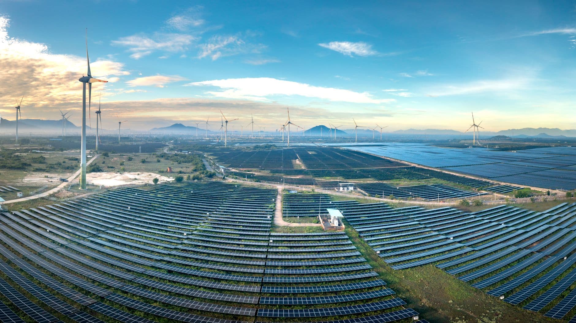 Aerial view of a solar and wind farm with rows of solar panels and wind turbines