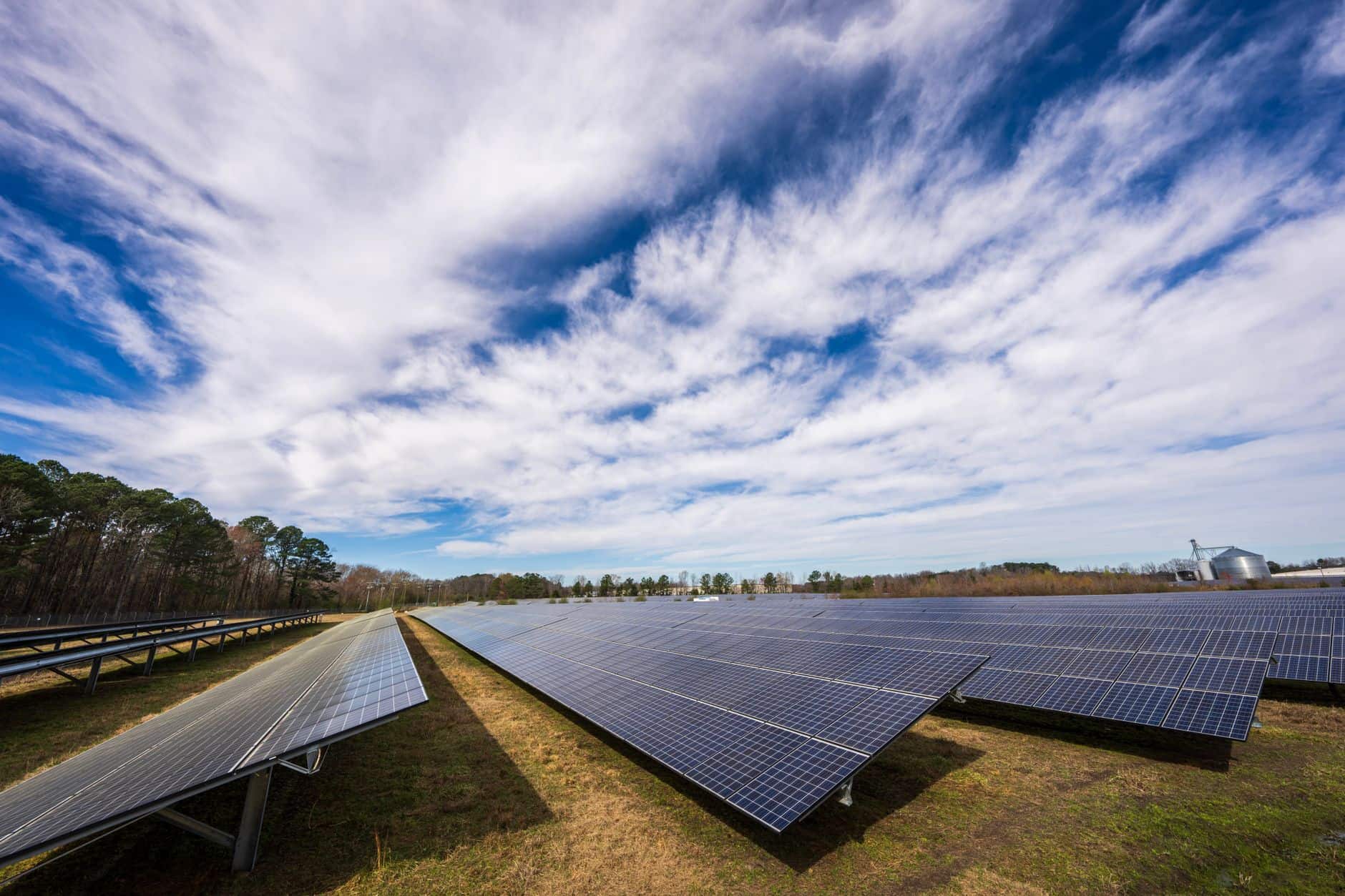 Solar panels covering a field under a bright blue sky with clouds