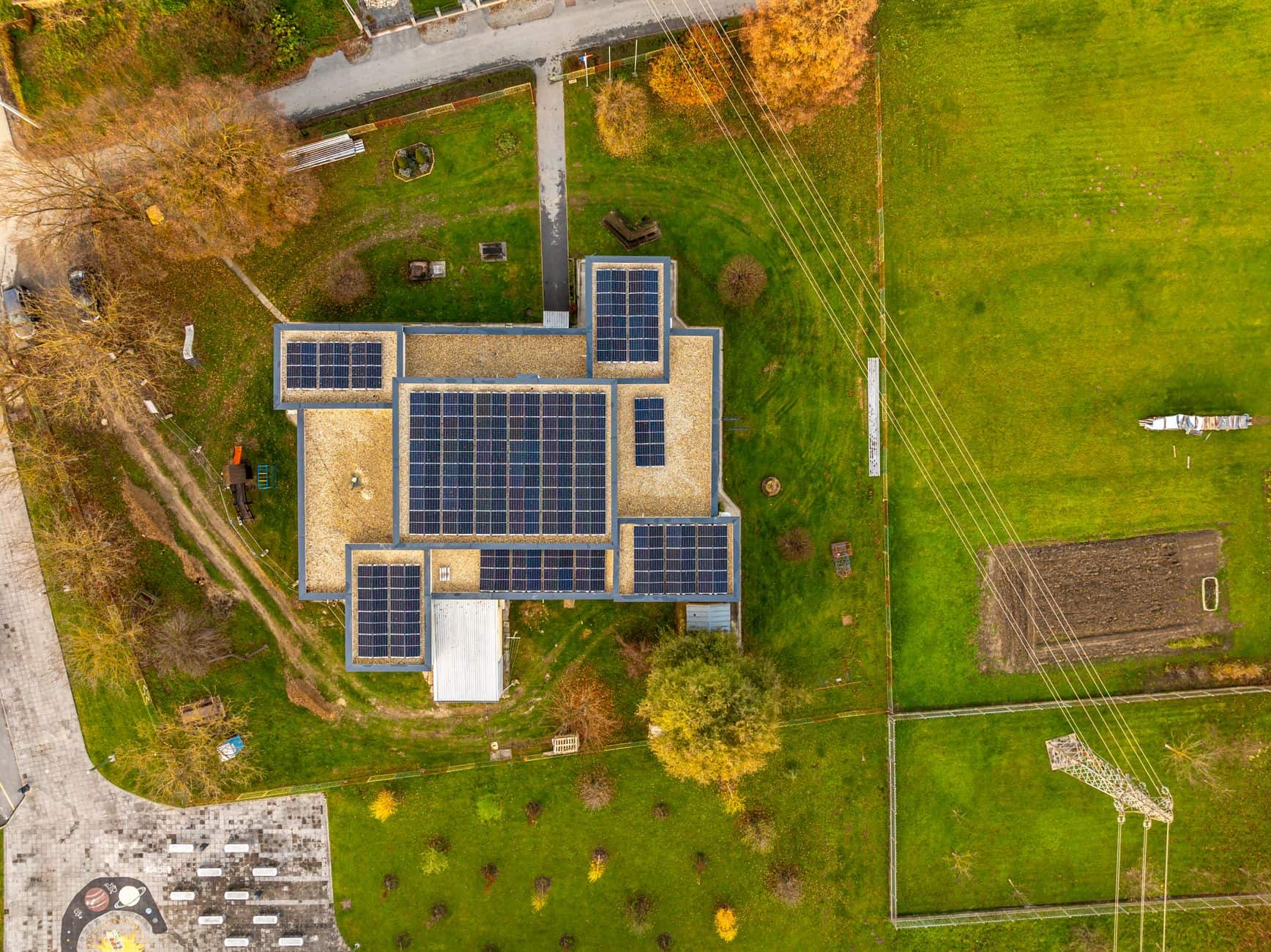 Aerial view of a building covered with solar panels surrounded by green landscape