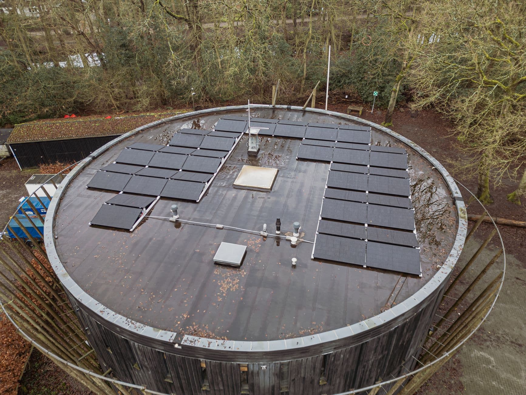 Overhead view of rooftop solar panels on a circular building surrounded by trees