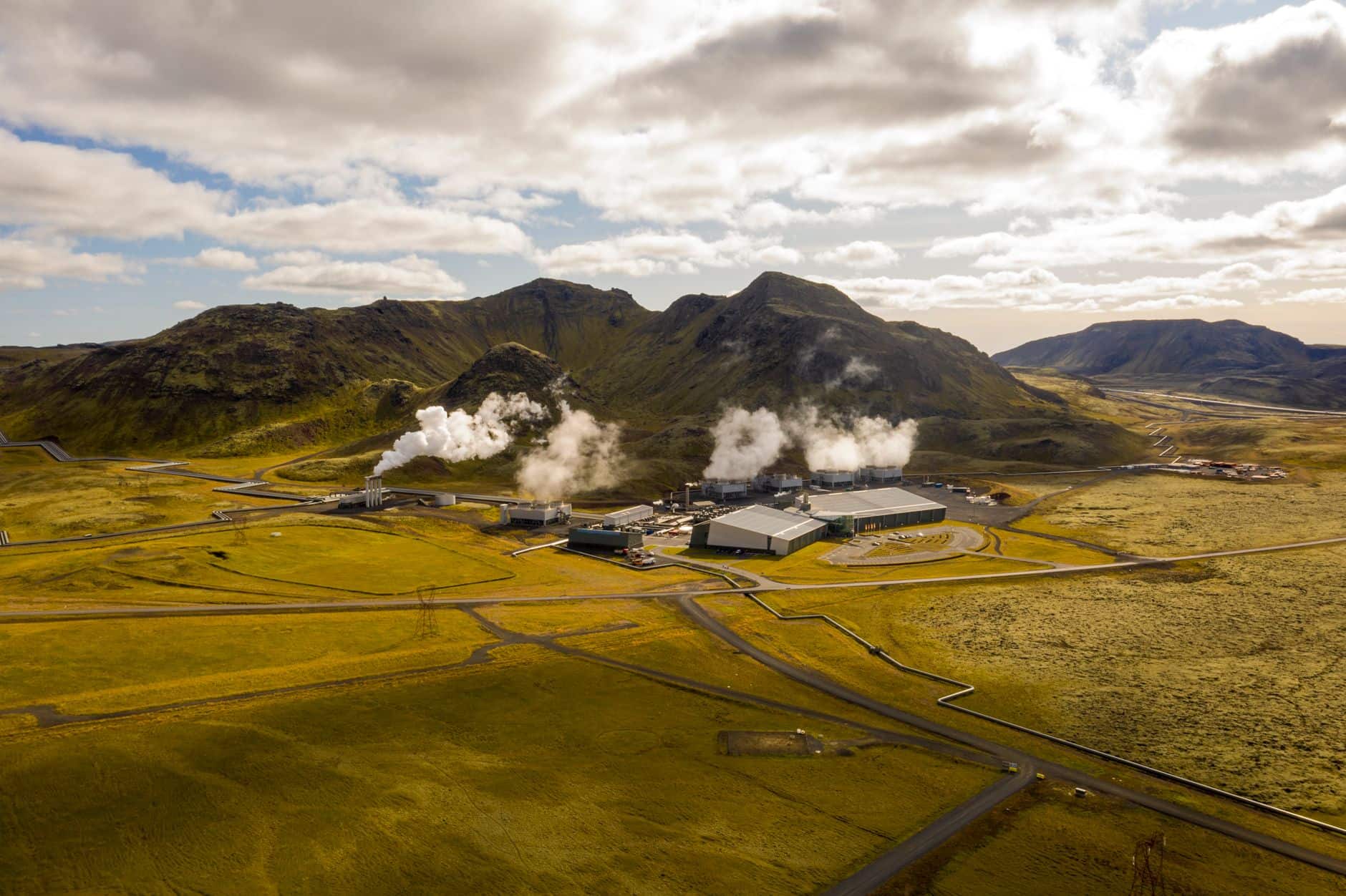 Aerial view of the Hellisheidi geothermal power plant in Iceland, showing steam plumes and surrounding mountains