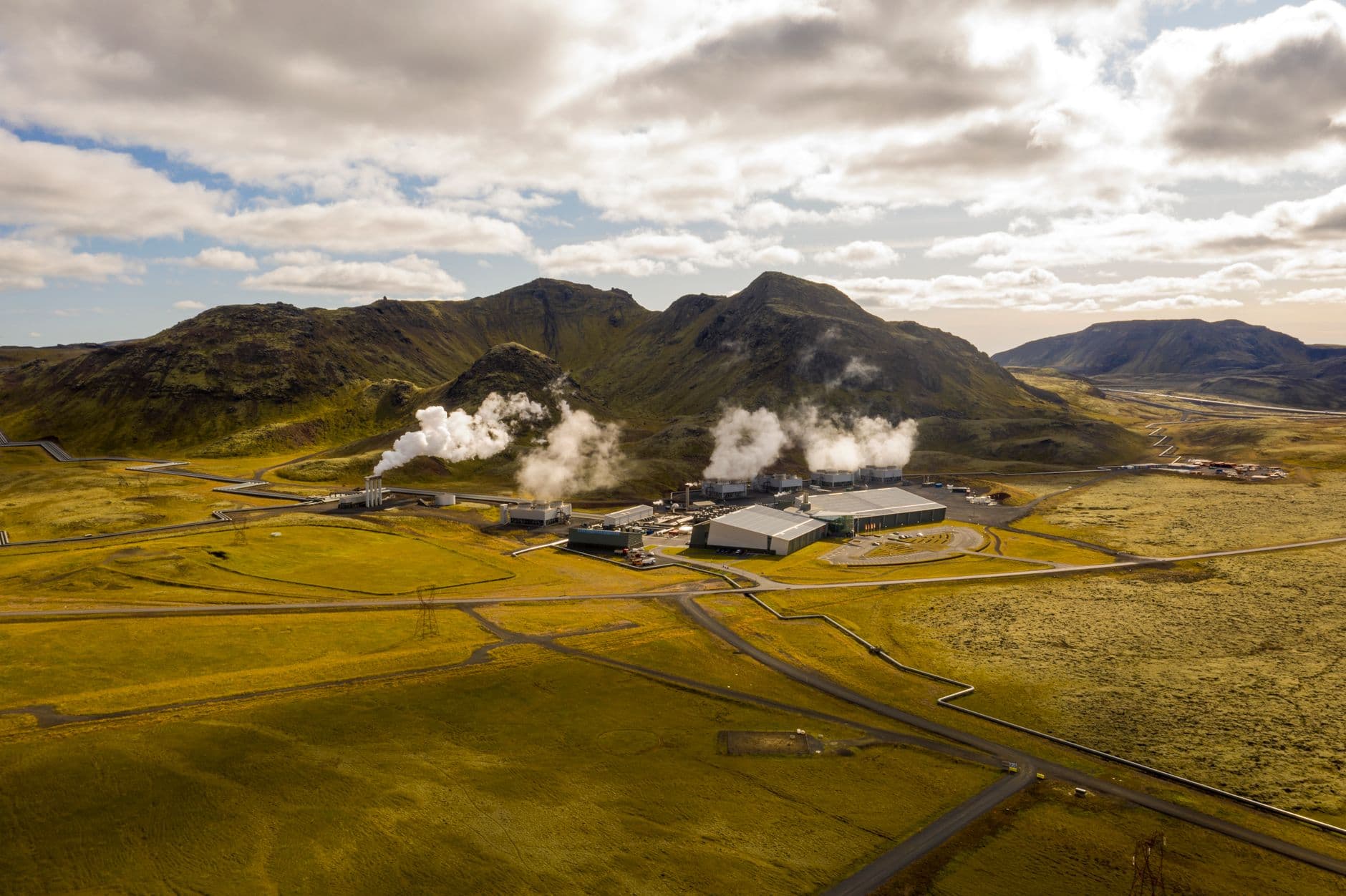 Aerial view of the Hellisheidi geothermal power plant in Iceland, showing steam plumes and surrounding mountains