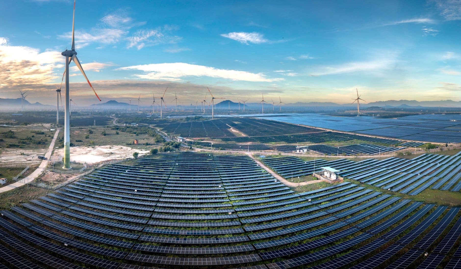 Aerial panoramic view of a solar farm with rows of solar panels under a clear sky