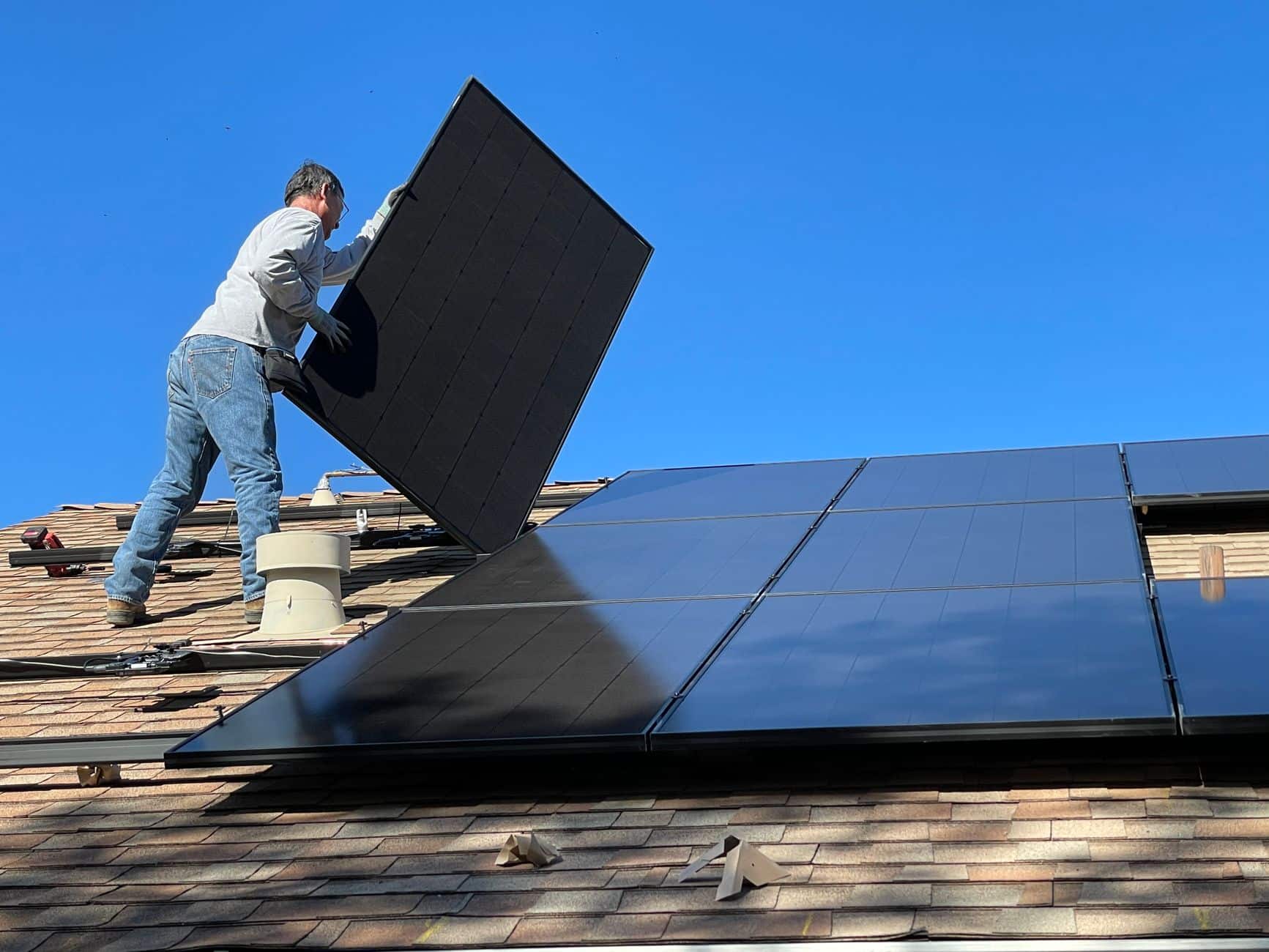 Worker installing solar panels on a rooftop under a sunny sky