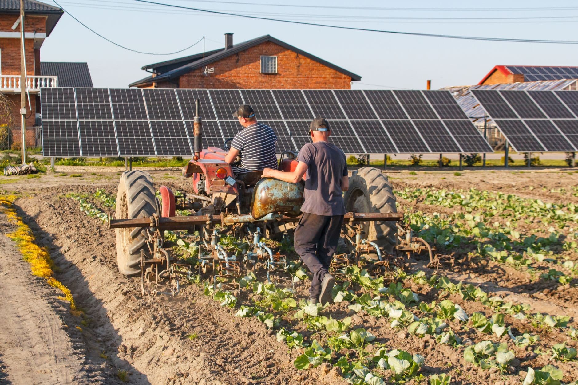 Farmers operating a tractor beside solar panels, illustrating modern sustainable agriculture