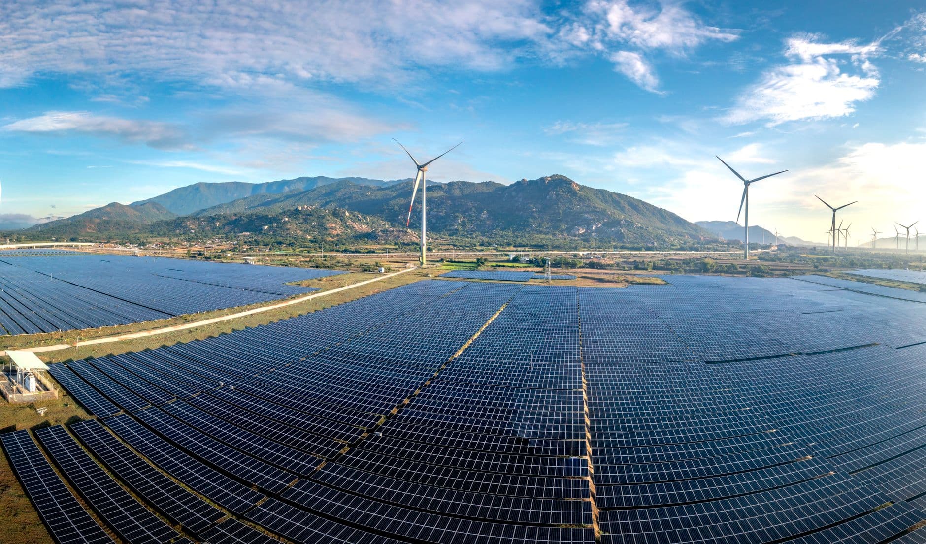Aerial view of a large solar farm with wind turbines on a sunny day