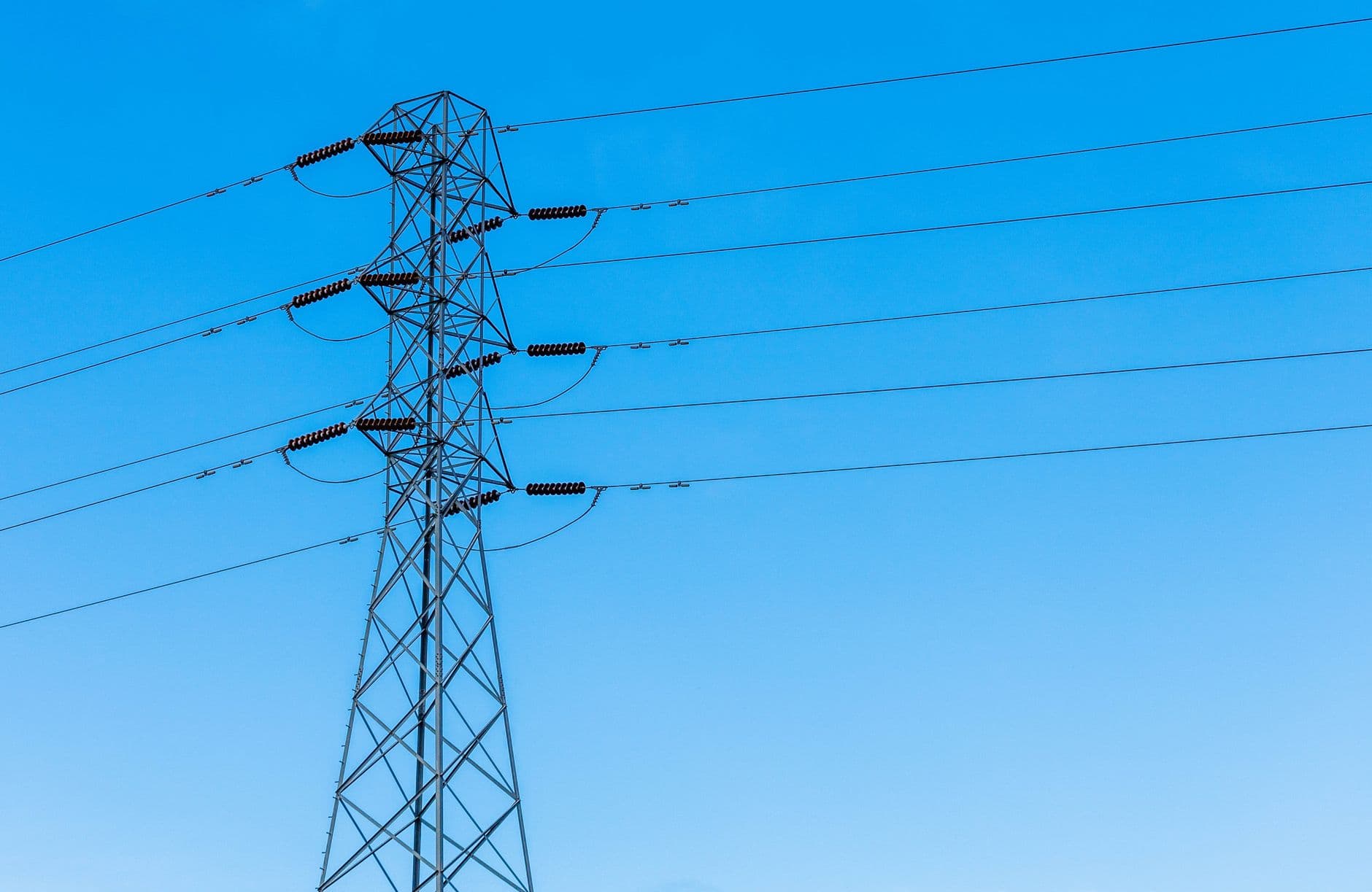 High voltage transmission tower with power lines under a bright blue sky