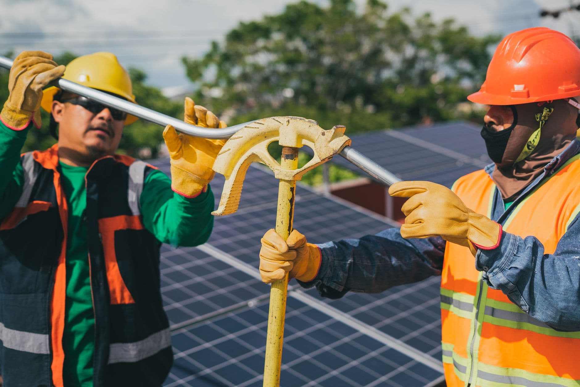 Two construction workers in safety gear assembling rooftop solar panels under a sunny sky