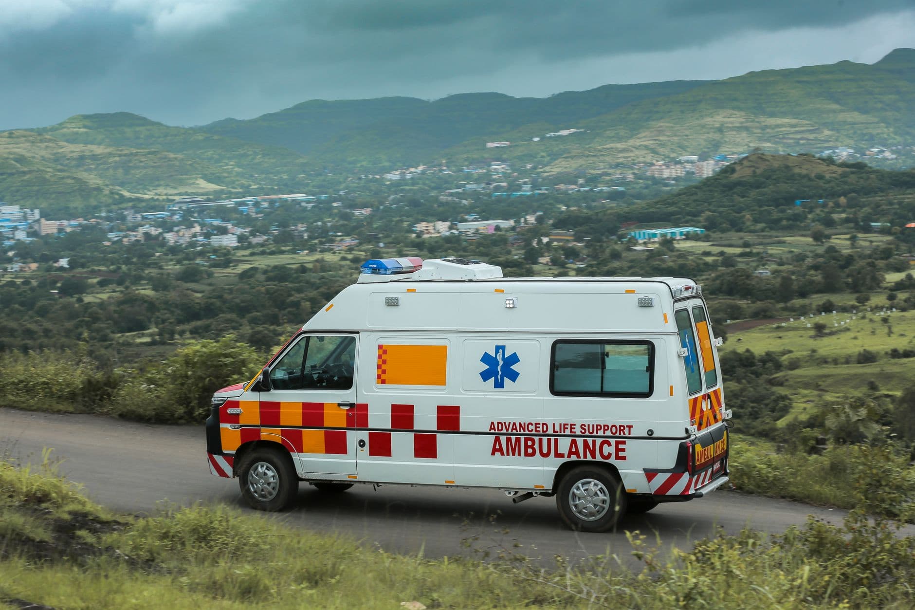 Advanced life support ambulance driving on a scenic road with green hills, highlighting solar-powered mobility