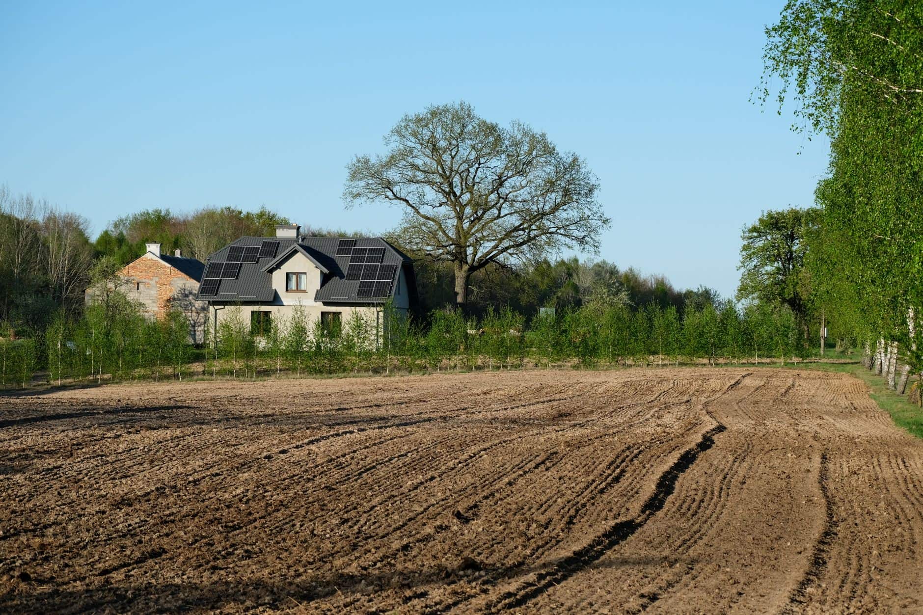 Rural house with solar panels surrounded by farmland and trees